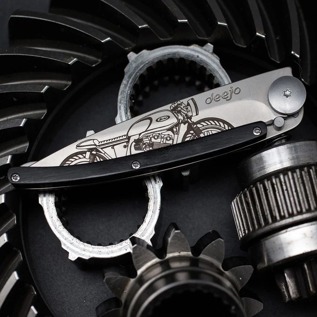 Complete closed Deejo Café Racer folding knife with motorcycle artwork and dark ebony-wood handle against an engine-gear backdrop