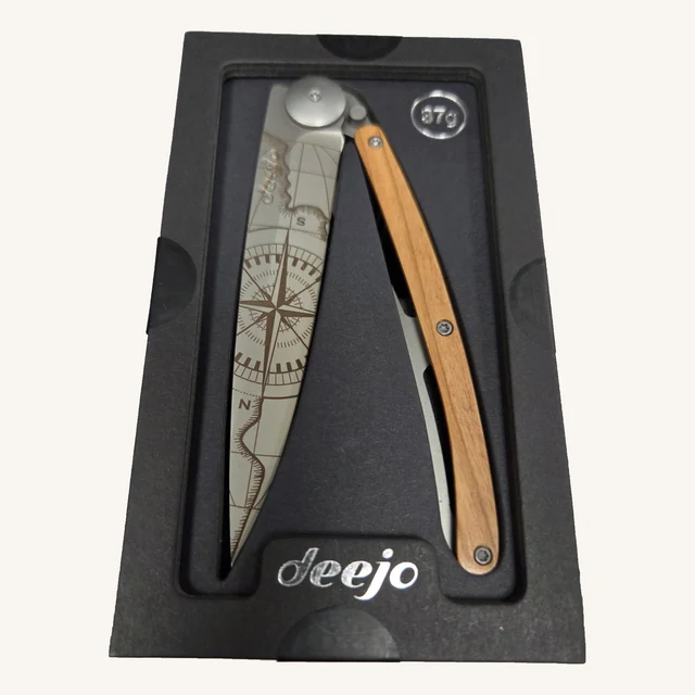 Deejo Terra Incognita 37g folding knife with an engraved compass-map blade and olive-wood handle in its black presentation tray