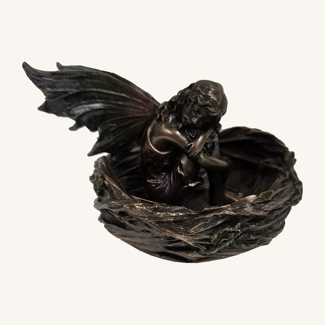 Bronze-colored fairy with a burgundy dress resting inside a round twig-textured nest with pointed wings and leafy accents
