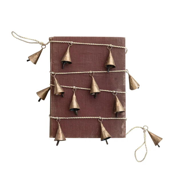 Gold-finished bell garland with white-and-gold twisted cord, styled around a brown book; the book is not included.