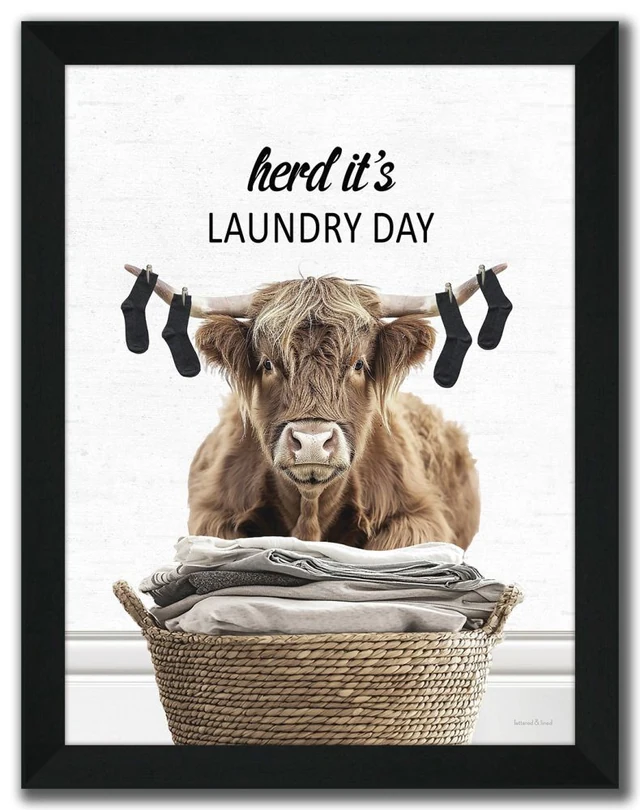 Complete black-framed Herd It’s Laundry Day artwork with a Highland cow, four socks hanging from its horns and a woven basket of linens
