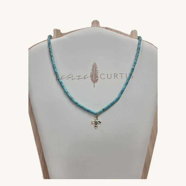 Jamie turquoise-blue heishi-stone necklace with a small ornate gold-tone cross pendant on its original Leslie Curtis display