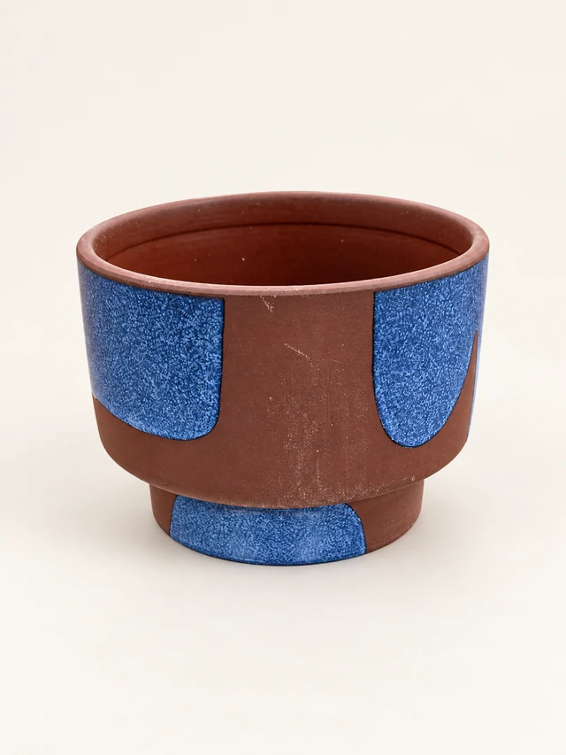 Round brown decorative pot with blue textured geometric panels and a raised base