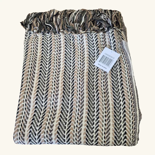 Folded Tasha recycled-cotton throw with its original black, cream and tan herringbone weave, complete fringed edge and printed product tag.