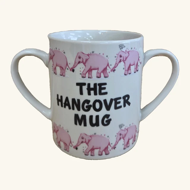 Cream-colored stoneware mug with two complete handles, rows of pink elephants and the original words THE HANGOVER MUG.