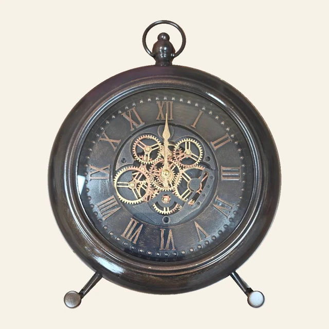 Venetian dark bronze-tone round table clock with Roman numerals, gold-tone central gears, a top loop, and two angled feet.