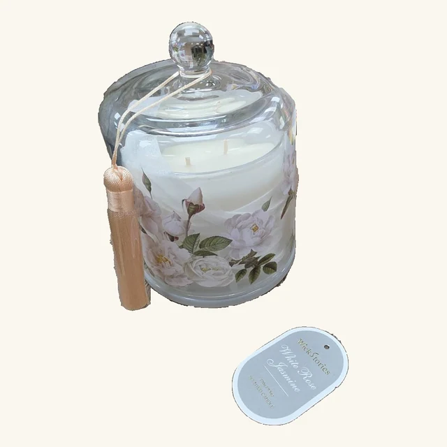 The complete White Rose Jasmine floral candle with its clear glass cloche, gold-colored tassel and original loose scent tag on a neutral background.